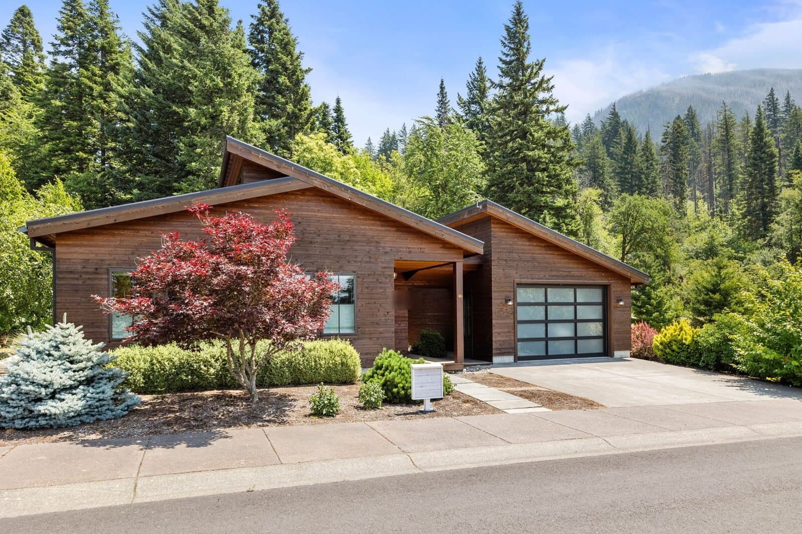 Listing photo: a low wood house with a glass garage door and a red maple in Cascade Locks