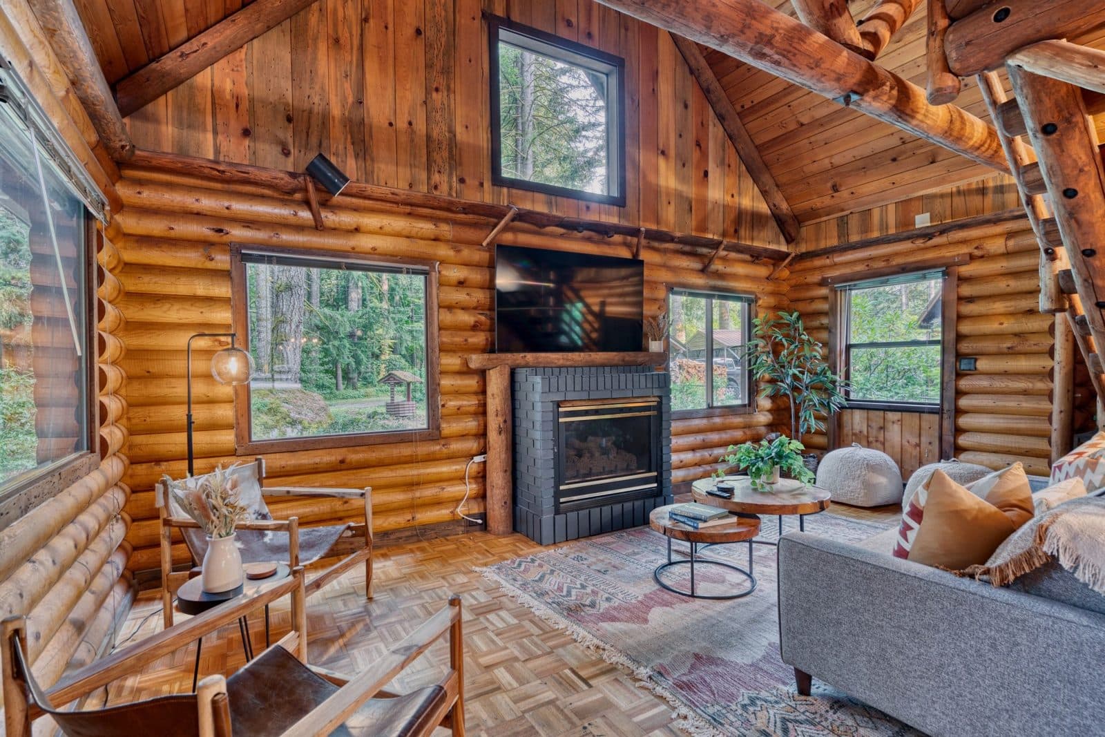 Listing photo: inside the log cabin, log walls, a gas fireplace and windows onto the trees