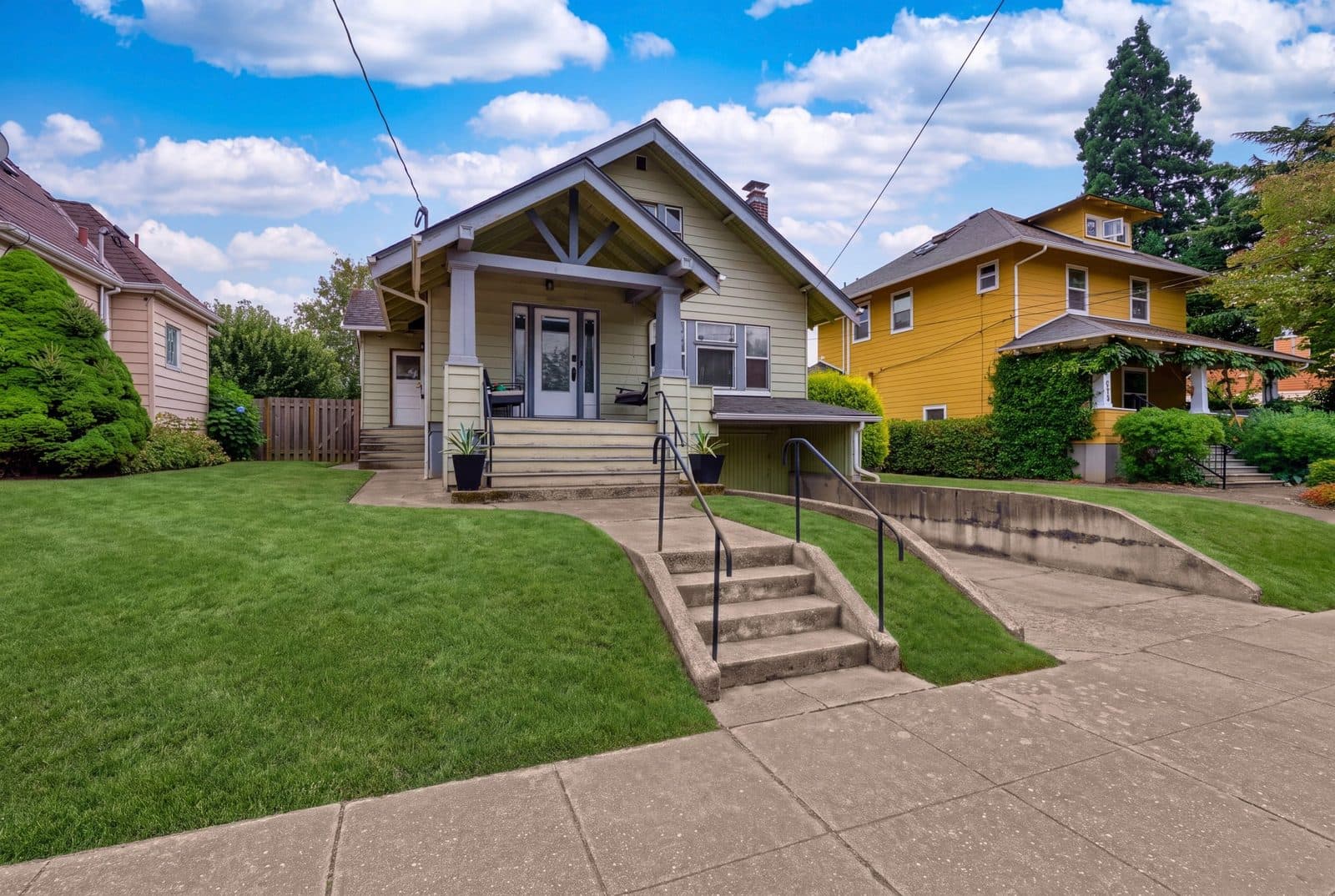 Listing photo: a sage Craftsman bungalow with a front porch, lawn and entry steps