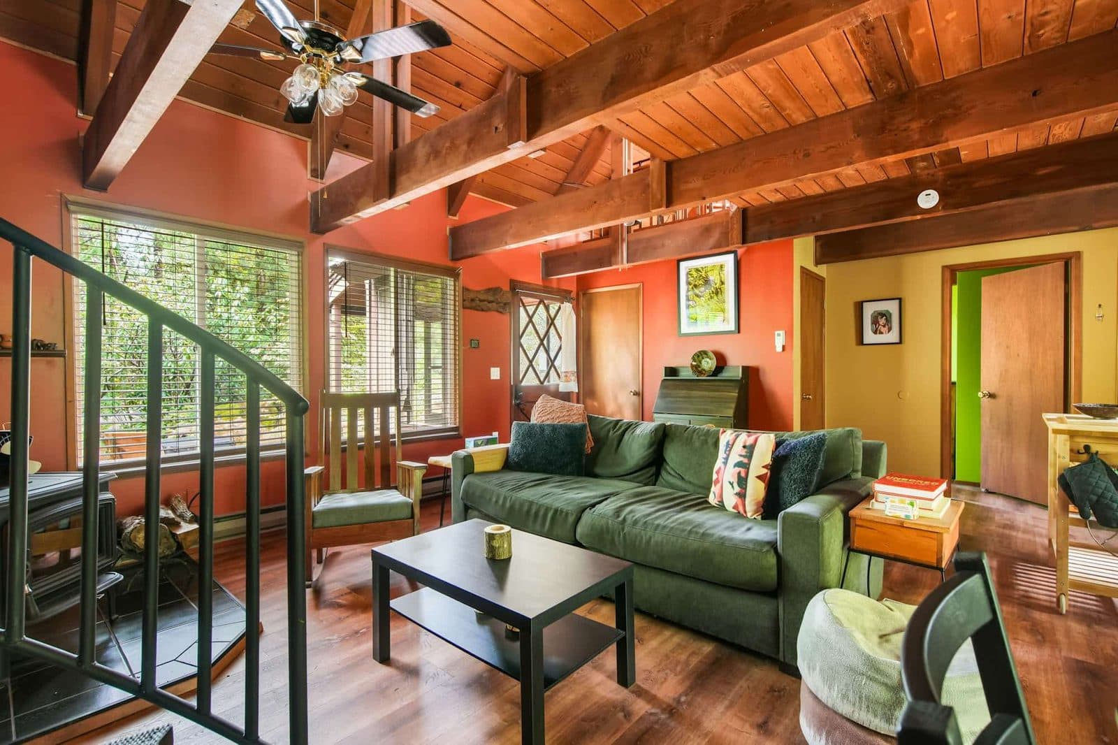 Listing photo: a cabin living room with red walls, a green sofa and a black spiral stair