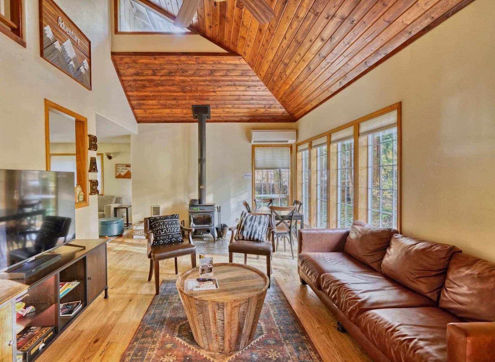Listing photo: a cabin living room with a wood stove, a leather sofa and tall windows